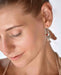 Close-up of a woman wearing silver earrings with a red gemstone against a neutral background