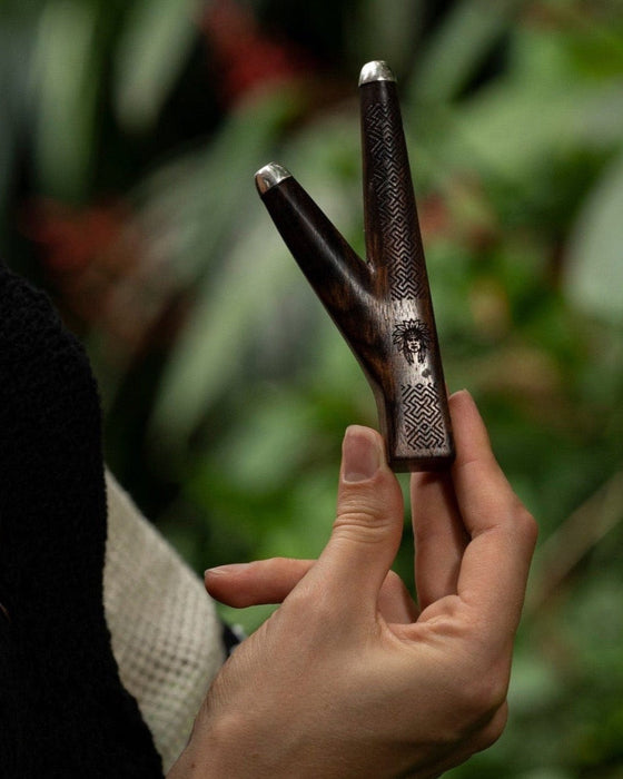 Elite rosewood kuripe pipe with intricate Shipibo patterns, held aloft, a sophisticated tool for hape snuff and a testament to shamanic craftsmanship.