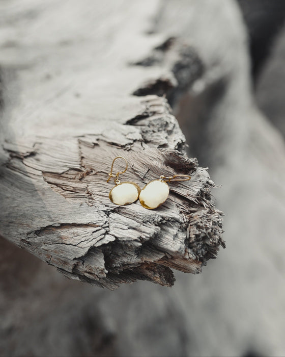 Hand-engraved bronze earrings featuring sacred geometry patterns, hanging against a rustic leather pouch