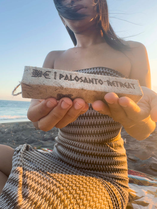 Person holding a Palo Santo retreat wooden block on a beach