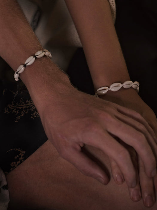 Close-up of hands wearing shell bracelets on a dark background