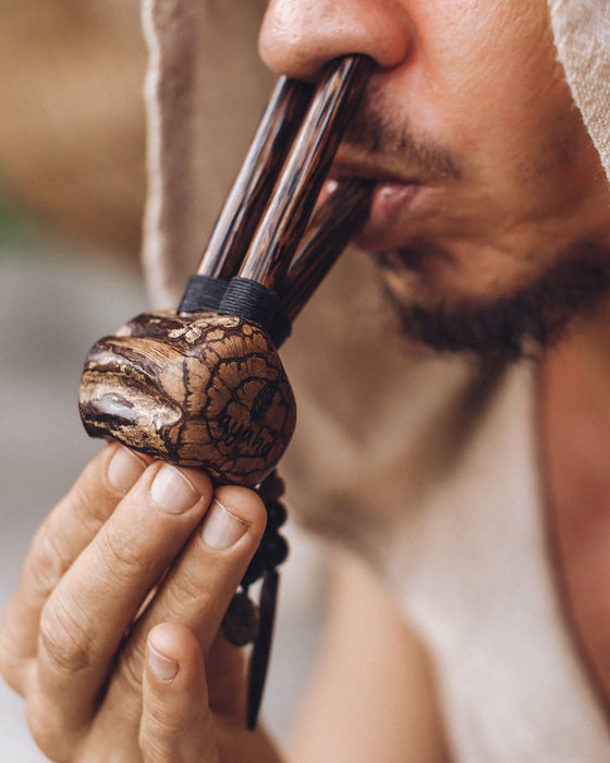 Person holding and blowing into a wooden pipe with a blurred background