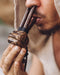 Person holding and blowing into a wooden pipe with a blurred background