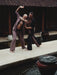 Two men practicing martial arts by a pool with traditional architecture in the background
