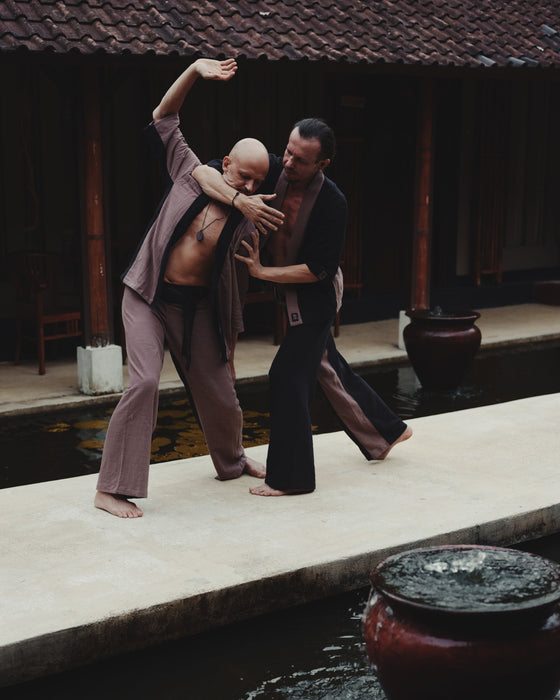 Two men practicing martial arts by a pool with traditional architecture in the background