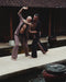 Two men practicing martial arts by a pool with traditional architecture in the background