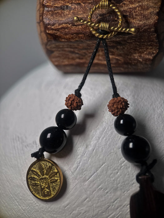 Black beaded necklace with a gold coin pendant on a textured surface