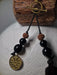 Black beaded necklace with a gold coin pendant on a textured surface