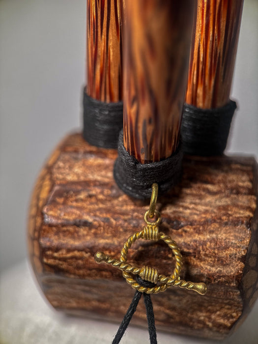 Wooden object with a gold ring and black cord on a textured surface