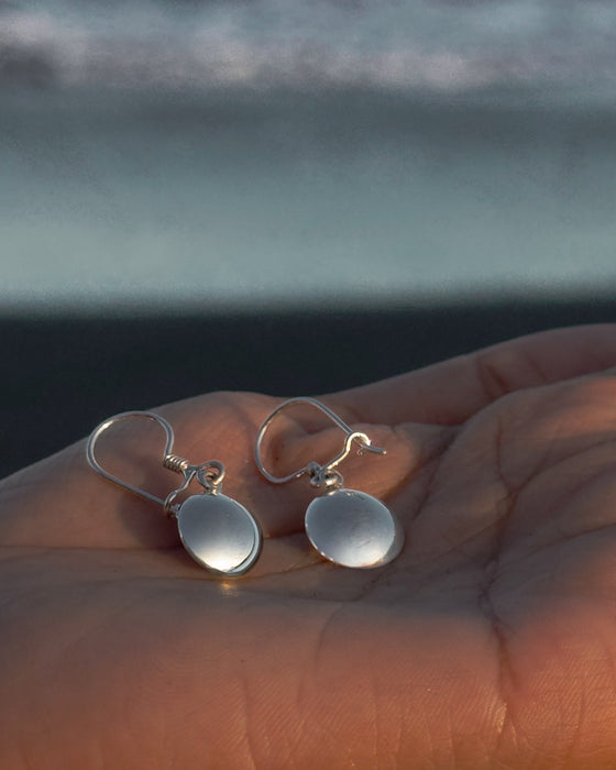 Silver earrings held in a hand with a blurred natural background