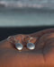 Silver earrings held in a hand with a blurred natural background