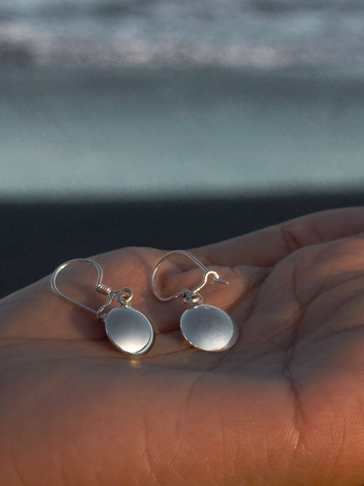 Silver earrings on a hand with a blurred ocean background