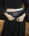 Person wearing a black outfit with a patterned belt against a blurred background