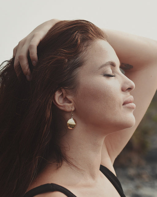 Bronze earrings with symbolic engravings and reflective mirrors, placed beside sage and crystals.
