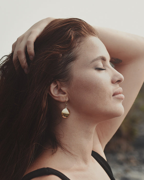 Bronze earrings with symbolic engravings and reflective mirrors, placed beside sage and crystals.