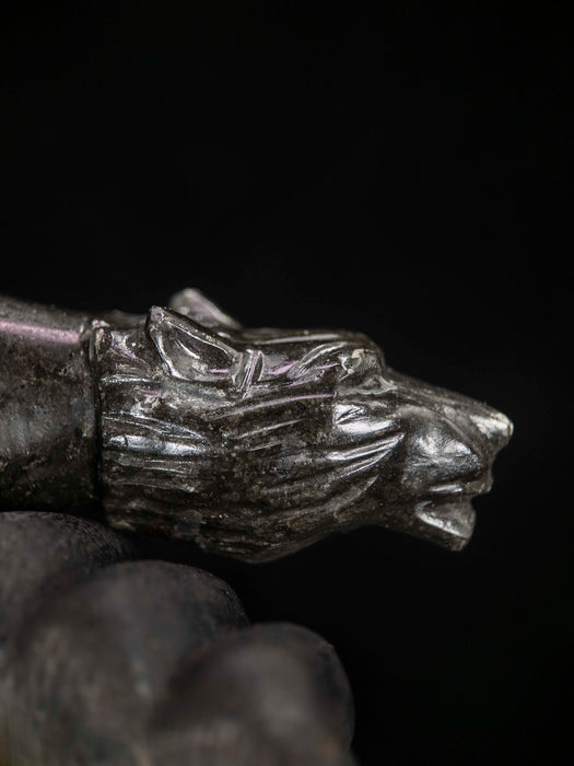 Metallic wolf head figurine held by a gloved hand against a dark background