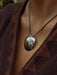 Close-up of a person wearing a textured pendant necklace with a brown patterned garment.
