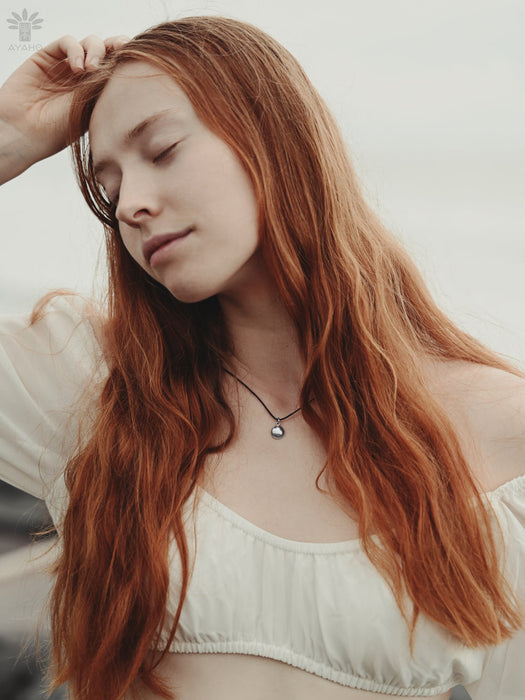 Woman with long red hair wearing a white top against a neutral background