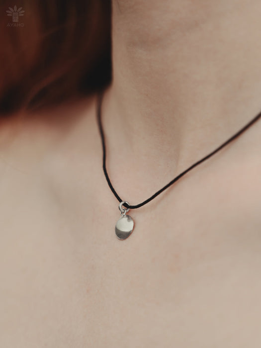 Necklace with a small pendant on a person's neck against a neutral background