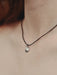 Necklace with a small pendant on a person's neck against a neutral background