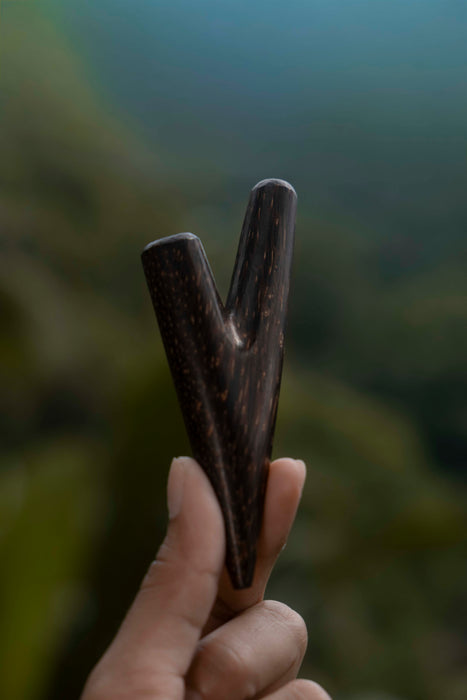 Hand holding a wooden arrowhead against a blurred natural background