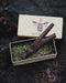 Wooden smoking tool on a bed of green moss with 'AYA' branding in the background