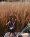 Wooden hand sculpture making a peace sign with a smoking stick in front of tall grass.