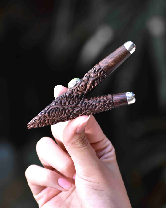 Hand holding a intricately carved wooden pen with a silver clip against a blurred background
