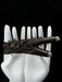 Decorative black object with intricate design on a white mannequin hand against a black background