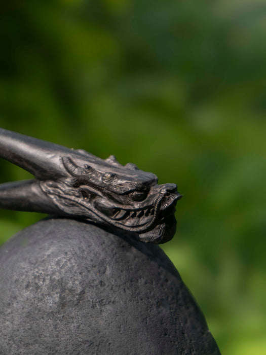 Close-up of a dragon head sculpture on a stone sphere with a blurred green background