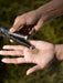 Hand holding a small object with another hand against a natural background