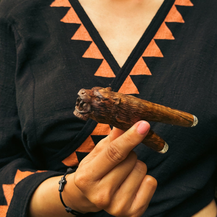 Person holding a wooden object with intricate carvings against a black and orange patterned background