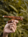 Hand holding a wooden and metal tool against a blurred natural background