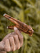 Hand holding a wooden object with a blurred natural background