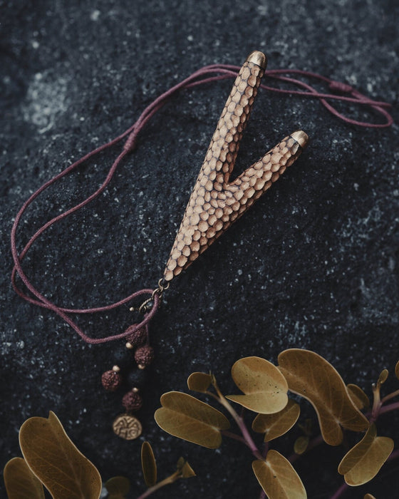 Golden Kuripe pipe, a ceremonial hape snuff applicator and shamanic tool, displayed as a necklace on weathered wood. Unique handmade smoking accessory for herbal medicine