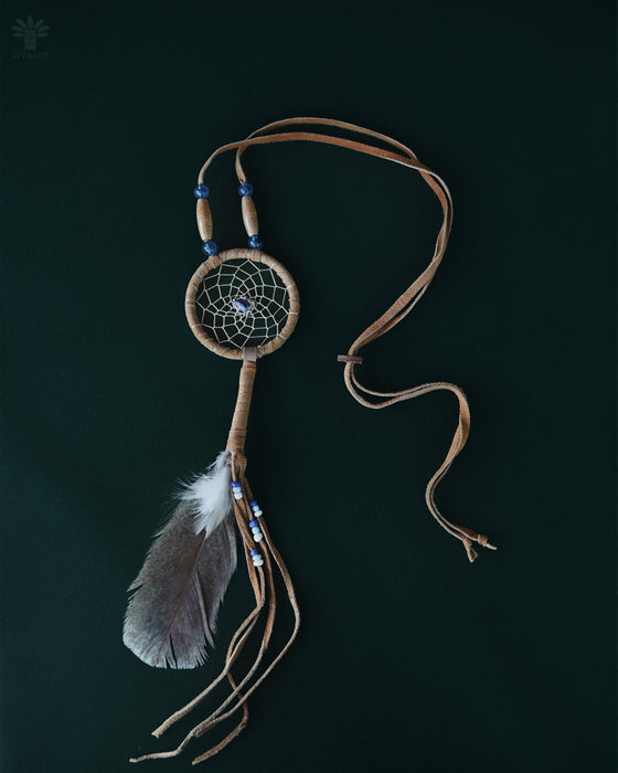 Tiny handcrafted dream catcher pendant on a leather cord, resting on a bed of dried lavender and crystals