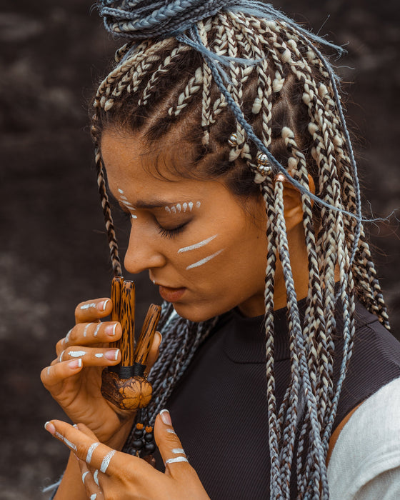 Woman with braided hair holding a wooden object against a dark background