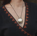 Person wearing a black top with a geometric pattern, featuring a necklace with a round pendant.