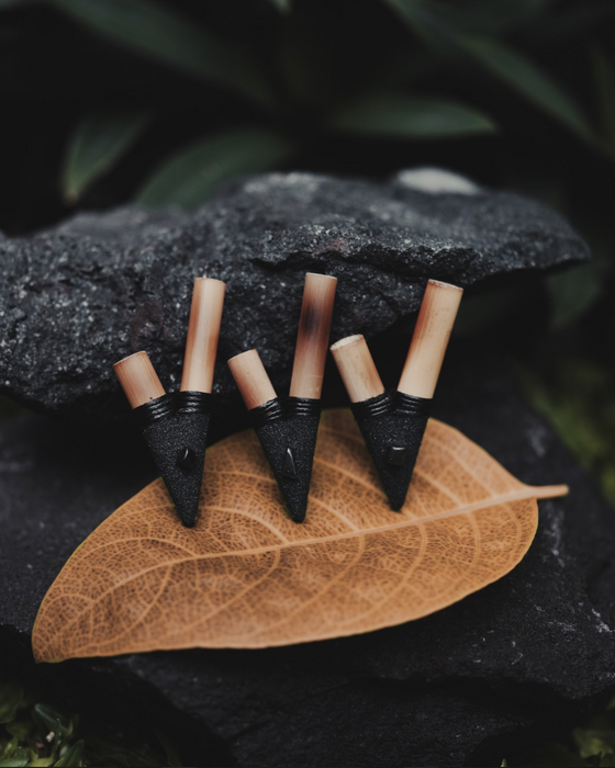 Five black and beige earrings on a brown leaf with a dark background