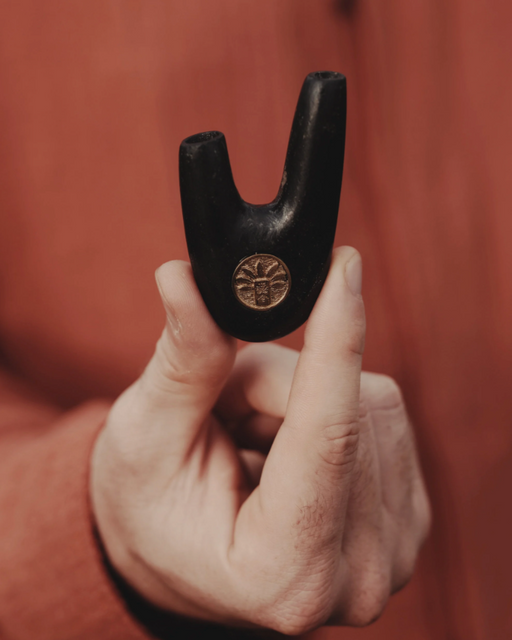 Hand holding a black metal tool with a logo against a red-brown background
