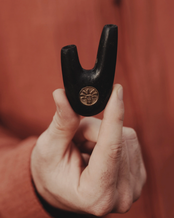 Hand holding a black metal tool with a logo against a red-brown background