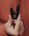 Hand holding a black metal tool with a logo against a red-brown background