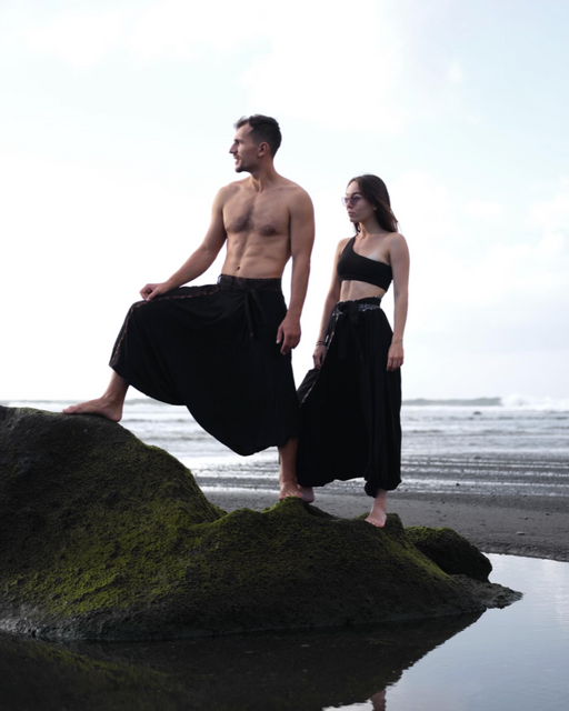 Two people in black outfits standing on a rock by the water, with 'Ayaho' logo in the corner.