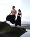 Two people in black outfits standing on a rock by the water, with 'Ayaho' logo in the corner.