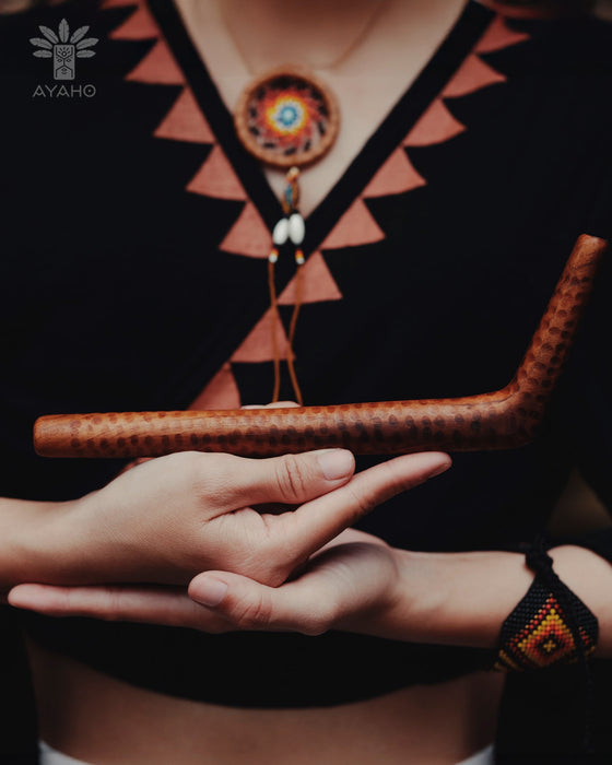 Person wearing a patterned top and holding a wooden object with Ayaro logo.