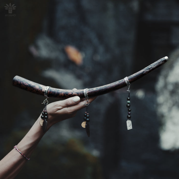 A person holding a shamanic Tepi, made of mango wood with bronze tips, over a natural outdoor setting.