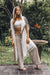 Woman in a white top and beige pants with a long white shawl standing outdoors.