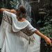 Woman in a white dress with a patterned shawl standing in front of a waterfall.