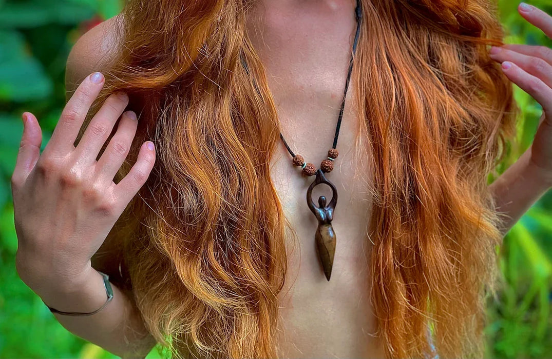 Person with long red hair and a necklace against a blurred green background