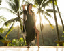 Woman in a black dress standing in front of palm trees with a sunset background
